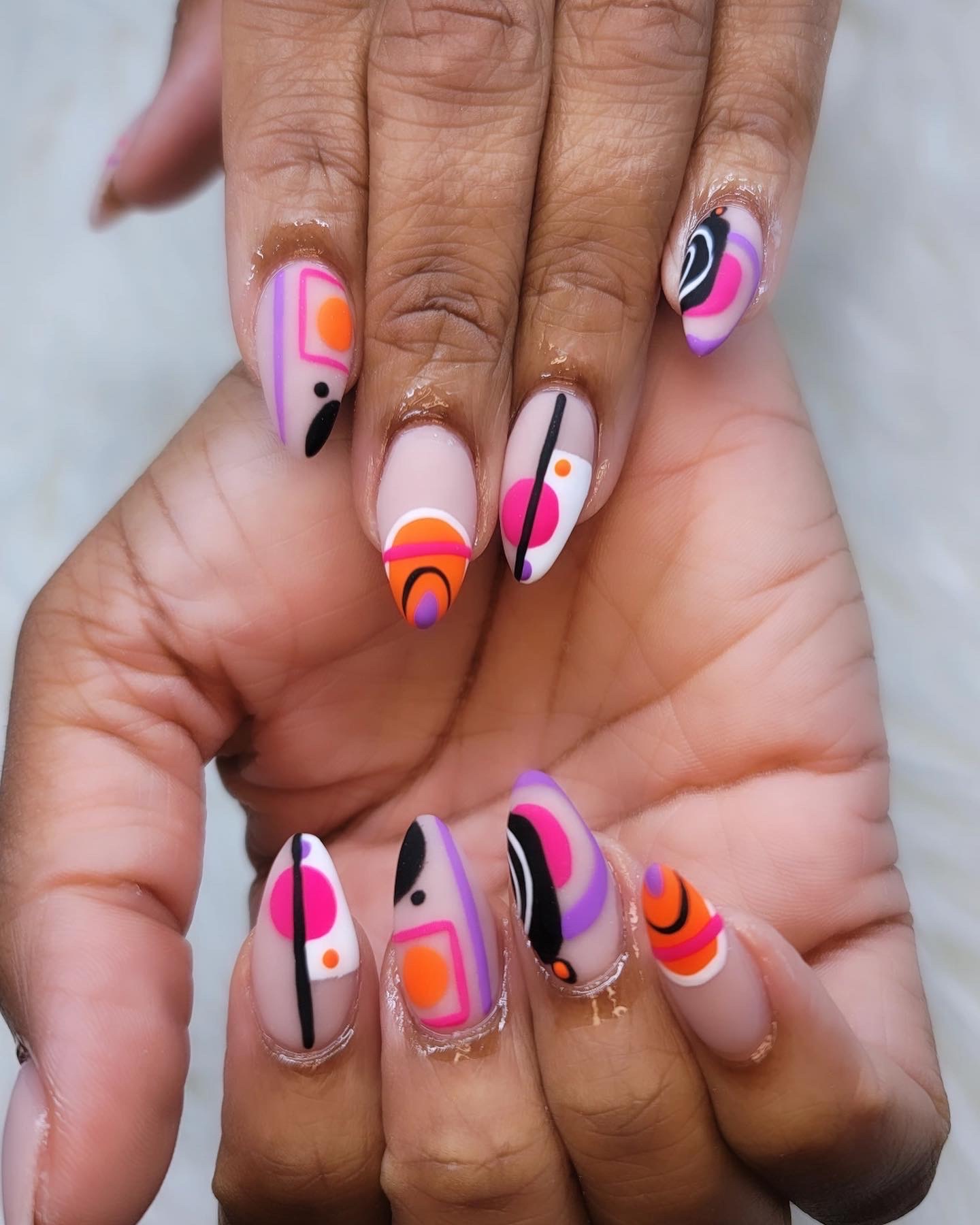 Almond nails painted with pink, orange, purple and black geometric shapes