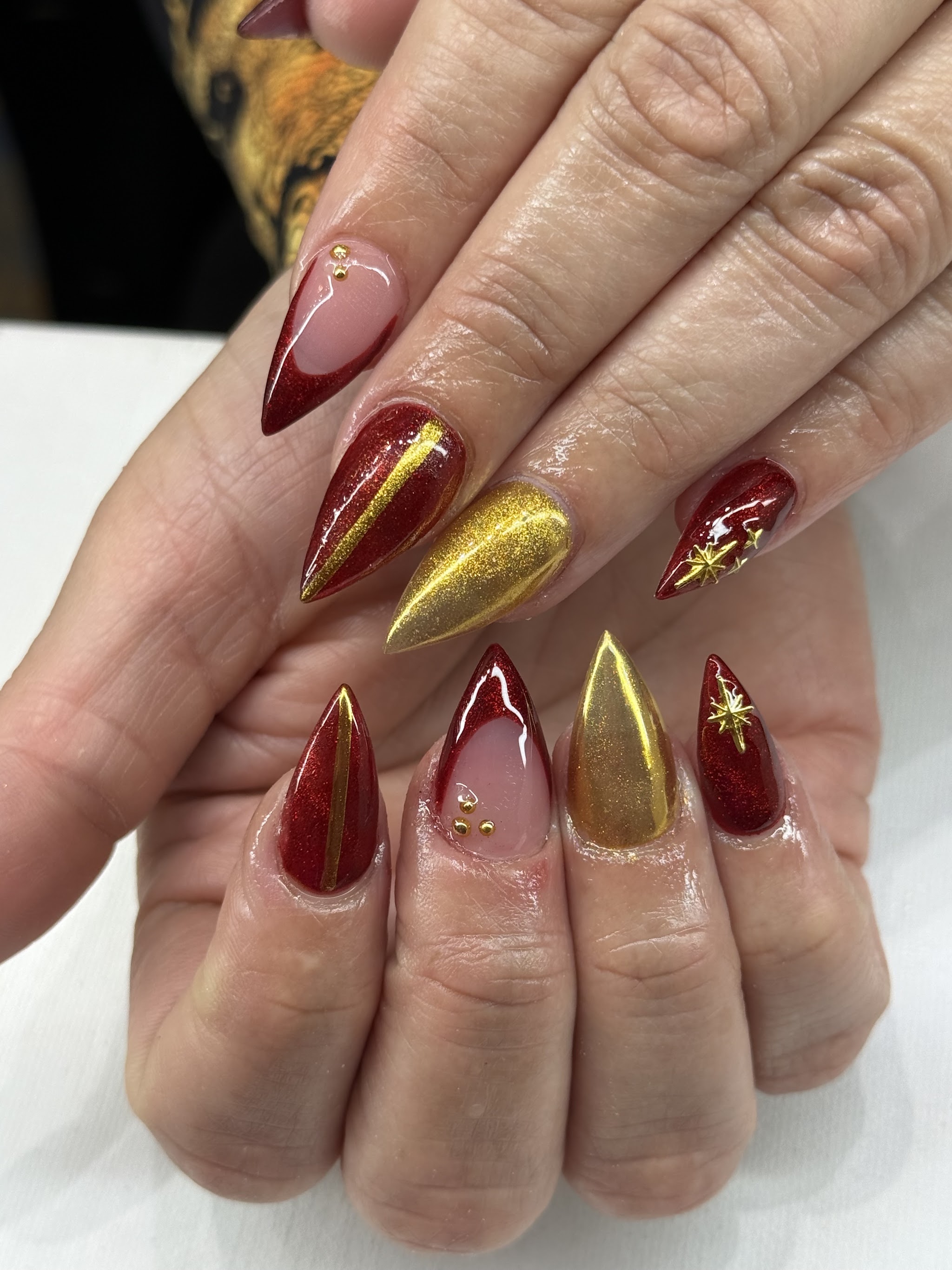 Pointed nails in deep red with gold chrome stripes and star details
